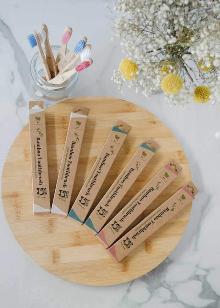 Bamboo toothbrushes in packaging on a wooden board with flowers in the background