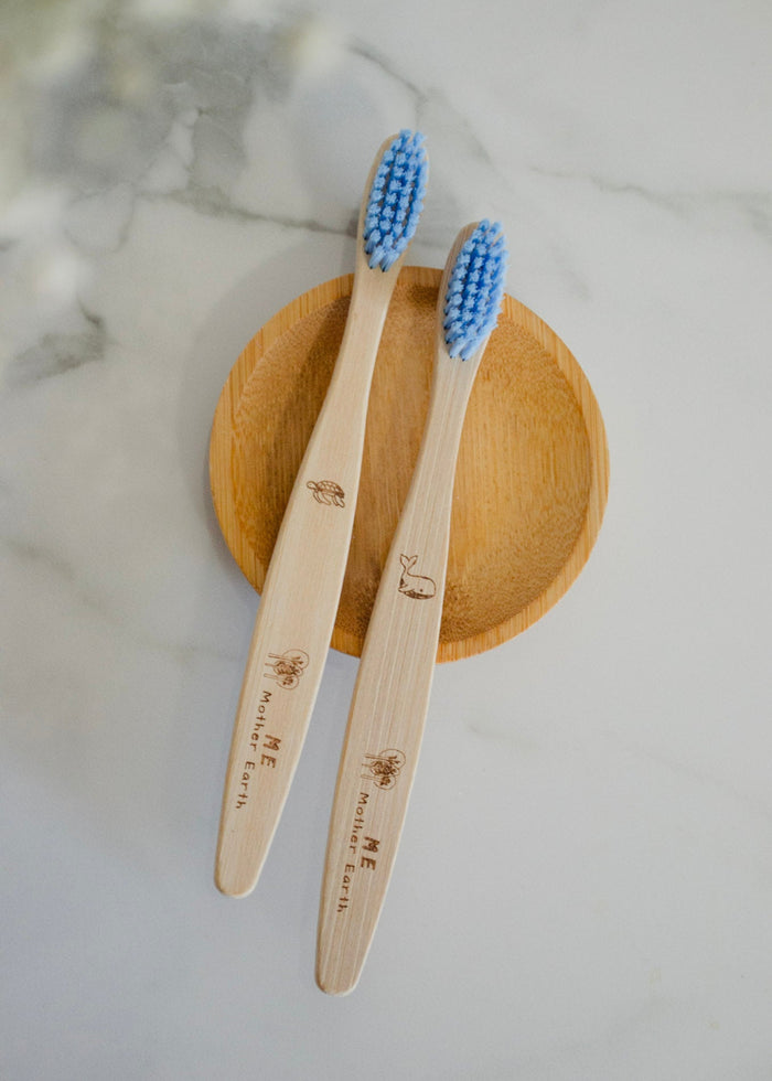 Two bamboo toothbrushes with blue bristles on a wooden stand against a marble background.