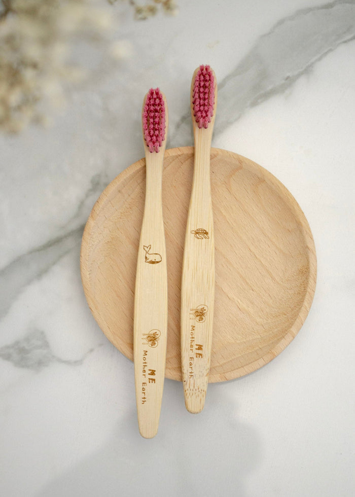 Two bamboo toothbrushes with red bristles on a wooden plate against a marble background.