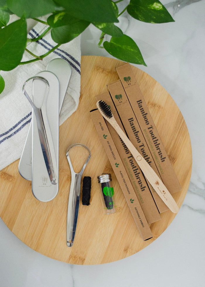 Set of bamboo toothbrushes and dental tools on a wooden board with greenery in the background.