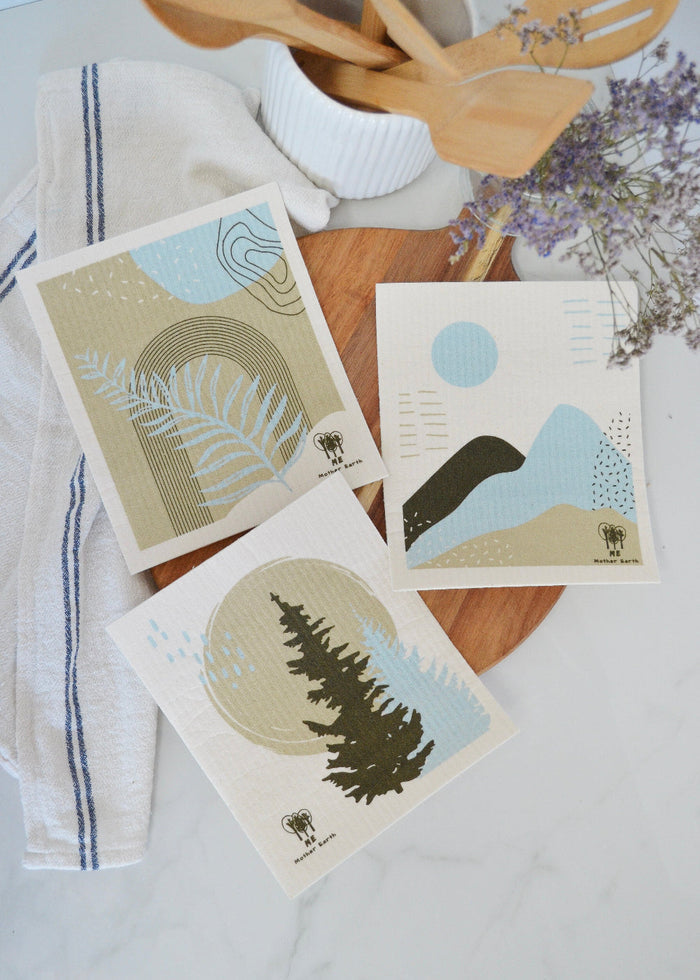 Three Swedish dishcloth with forest nature-themed designs on a wooden surface.
