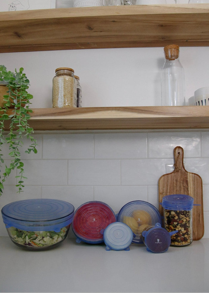 Kitchen counter with bowls, using Silicone bowl covers a cutting board, and wooden shelves with kitchen items.