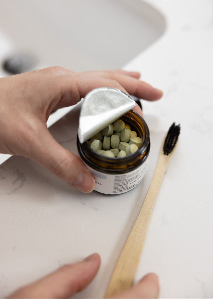 Person holding a amber glass jar of green Mouthwash capsules on a white countertop.