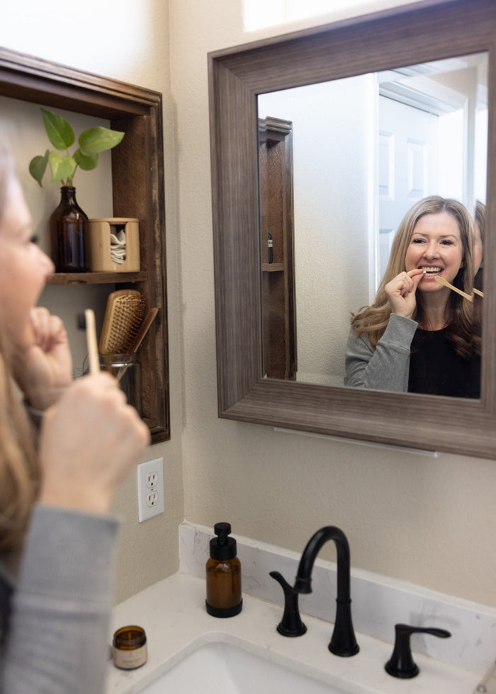 Woman brushing her teeth in front of a bathroom mirror with a wooden frame.