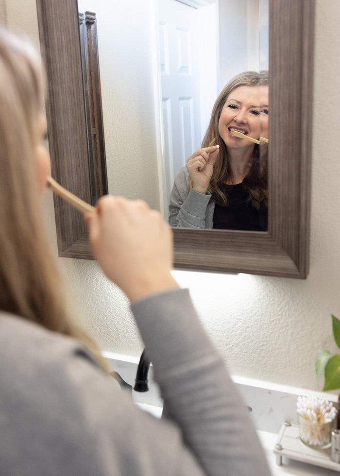 Woman brushing her teeth in front of a bathroom mirror.